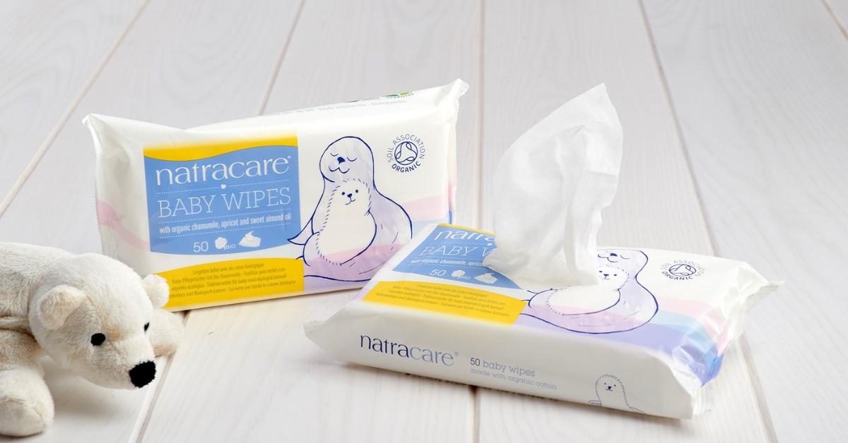 Two packages of Natracare baby wipes on white wooden floor next to bear toy